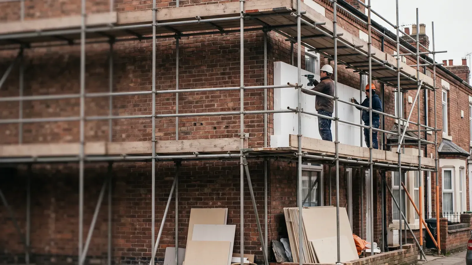 Installers fixing external wall insulation boards to a solid brick terraced house