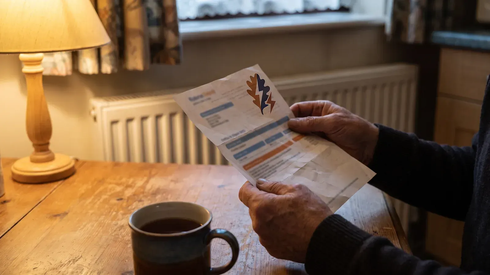 Householder holding a winter electricity bill at the kitchen table, the bill the Warm Home Discount takes £150 off